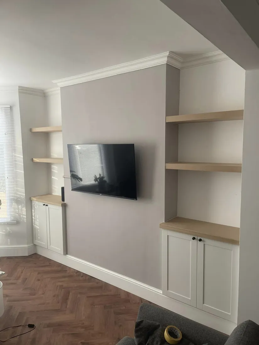 Fitted alcove media wall with white shaker cupboards, oak floating shelves and a wall-mounted TV